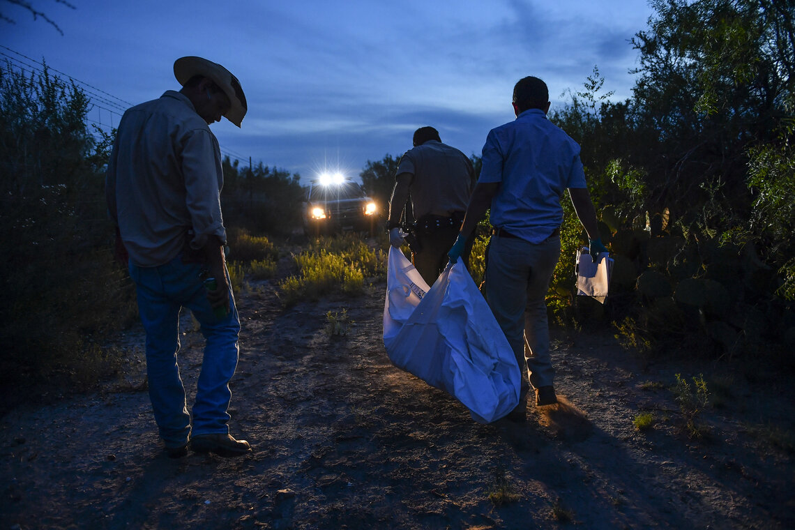 Ranch hand Juan Ramirez, left, looks on as Webb County Sheriff's Deputy Mauro Lopez, front, and Webb County Medical Examiner's Office investigator, Max Cantu, right, carry away the remains of a border crosser from a Laredo, Texas ranch, in 2016.