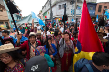 A crowd of indigenous people in Guatemala, in the street, indigenous authorities raising their sacred stick.